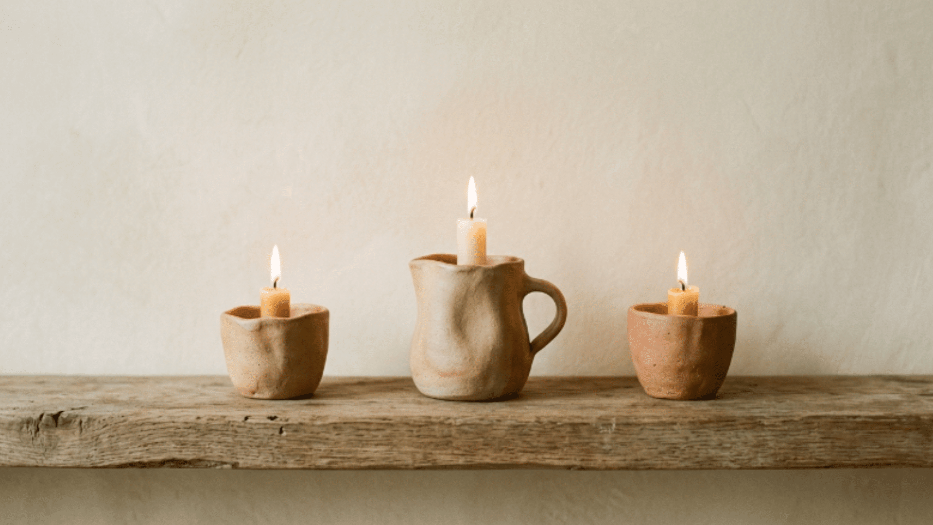 handmade clay candle holders displayed on a wooden shelf with warm lighting