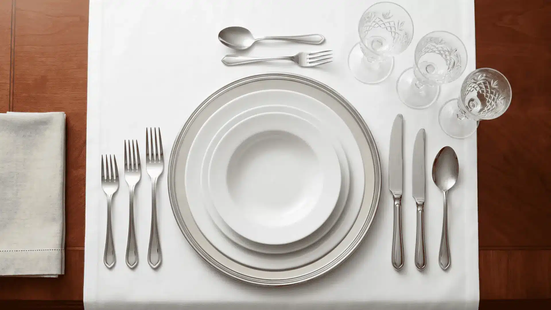 A formal table setting with a charger plate, flatware arranged outside-in, and glassware on the upper right.