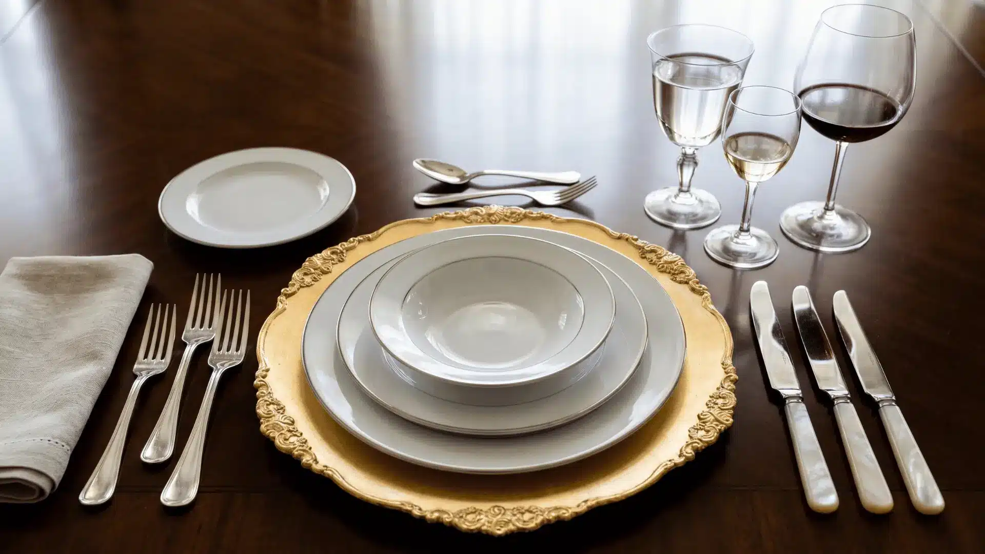 A formal table setting with charger plate, dinner plate, stacked soup and appetizer plates, flatware arranged by use, dessert utensils above the plate, and glassware placed to the right.