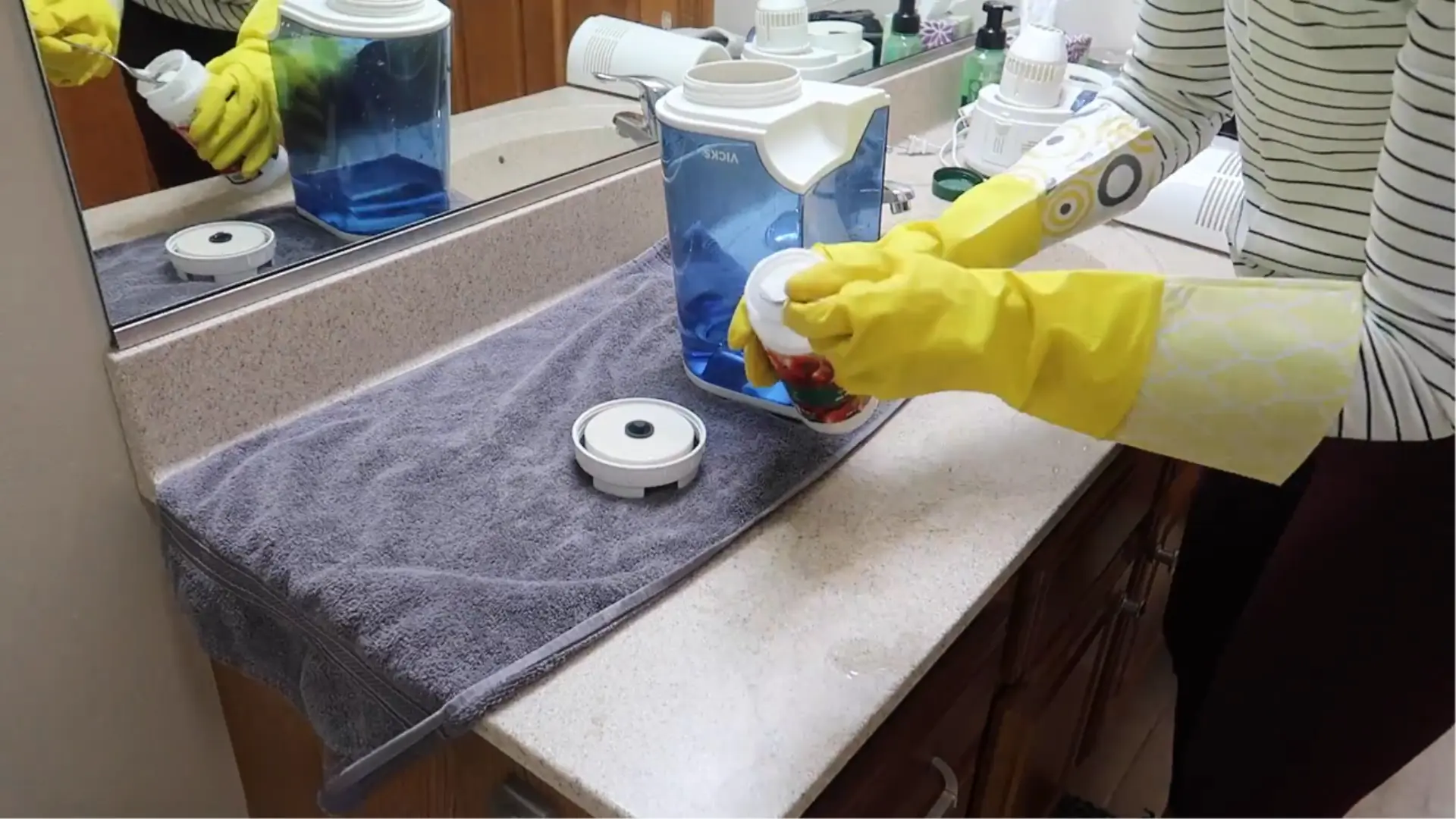 Person wearing yellow gloves adding citric acid powder to a humidifier part beside the water tank.