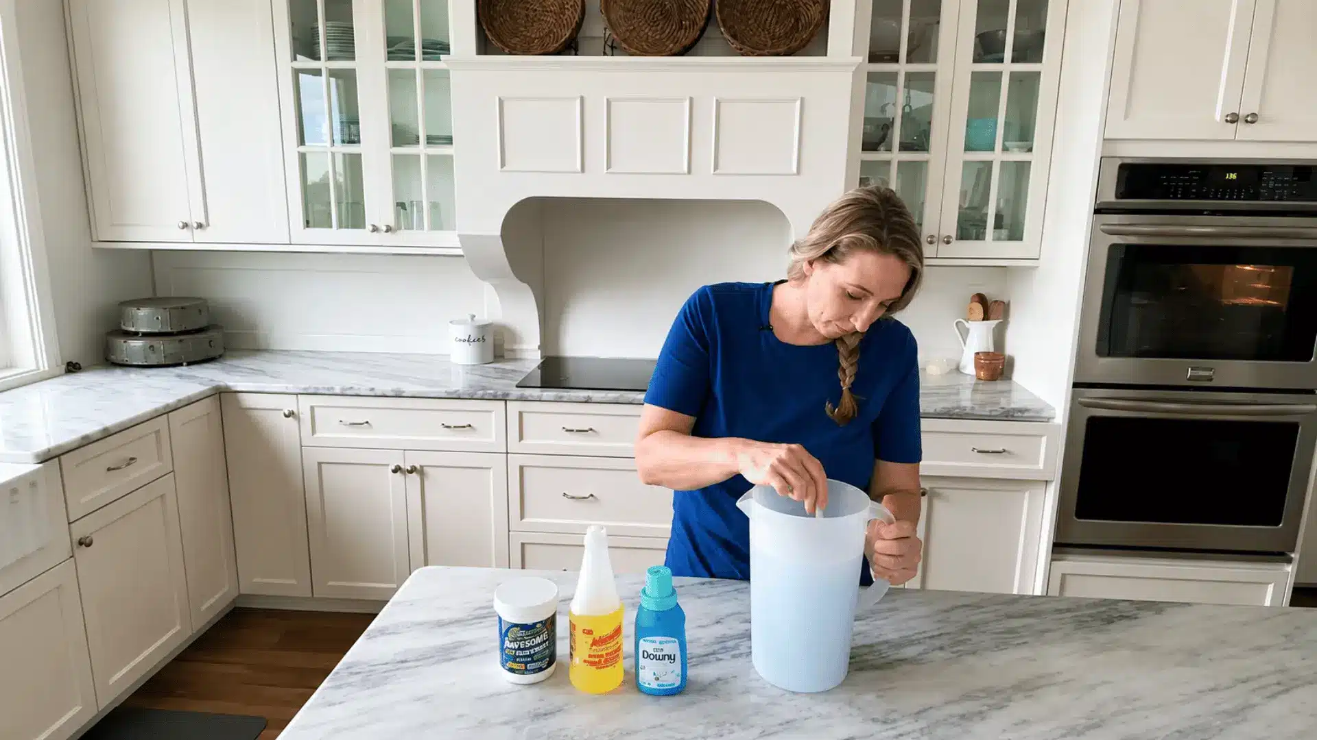 Person mixing homemade carpet cleaning solution in a large pitcher on a bright kitchen countertop with cleaning ingredients nearby.
