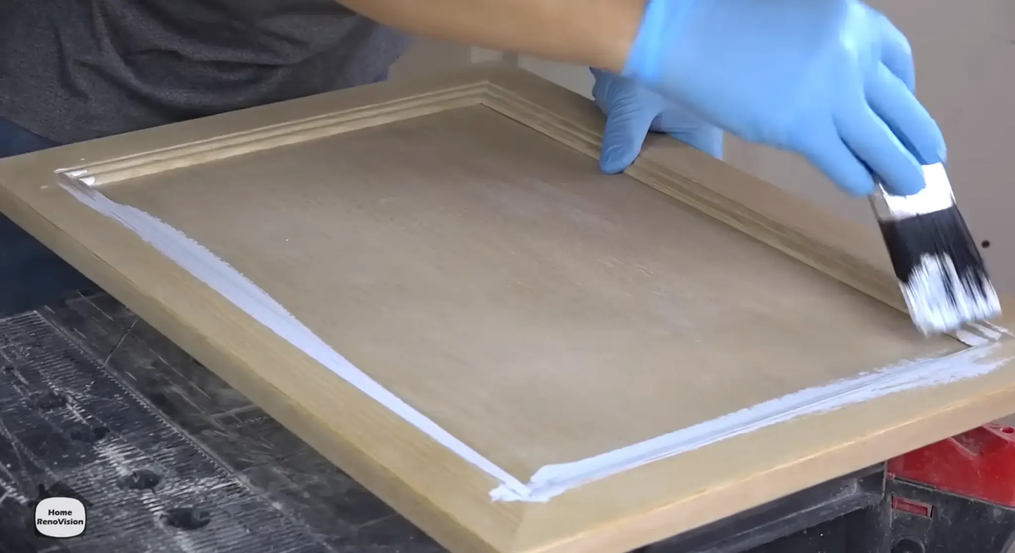 Applying the first coat of cabinet paint to a wooden kitchen cabinet door with an angled brush.