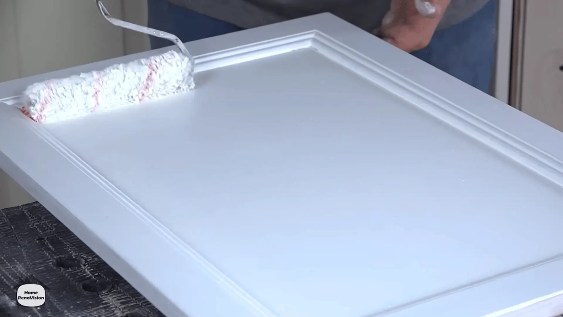 Applying a second coat of white cabinet paint to a wooden kitchen cabinet door with a brush.