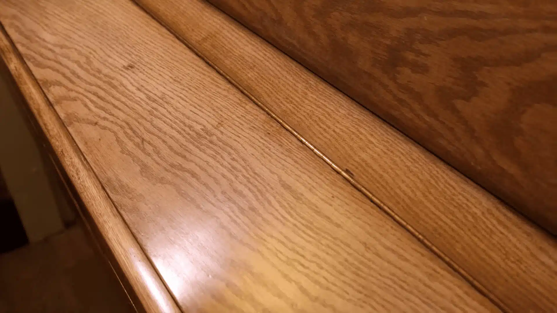 Close-up of wooden surface with visible grain and a thin brass seam detail between two joined panels.