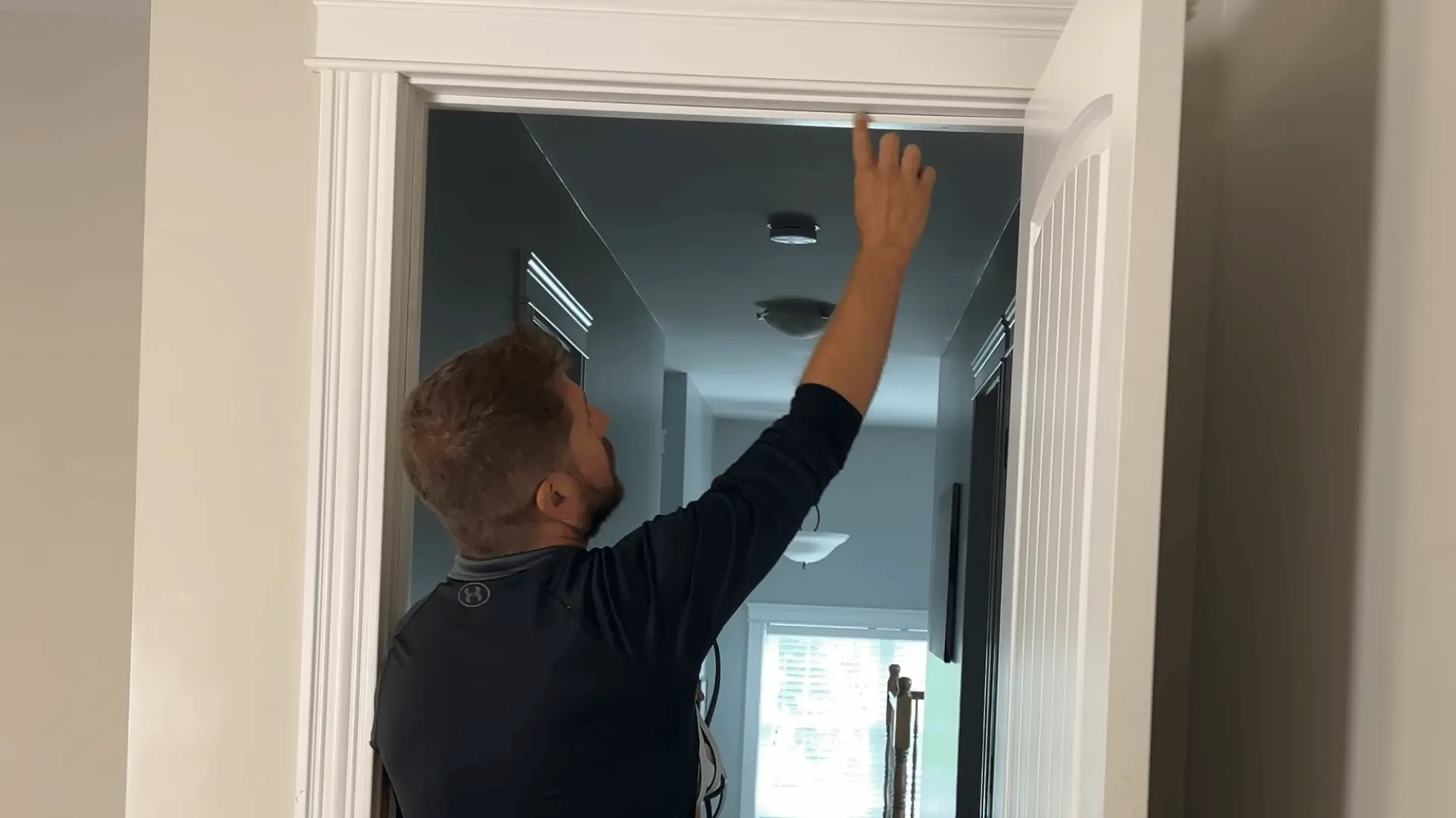 A man reaches up to clean the top frame of an open white interior door before applying a seal.