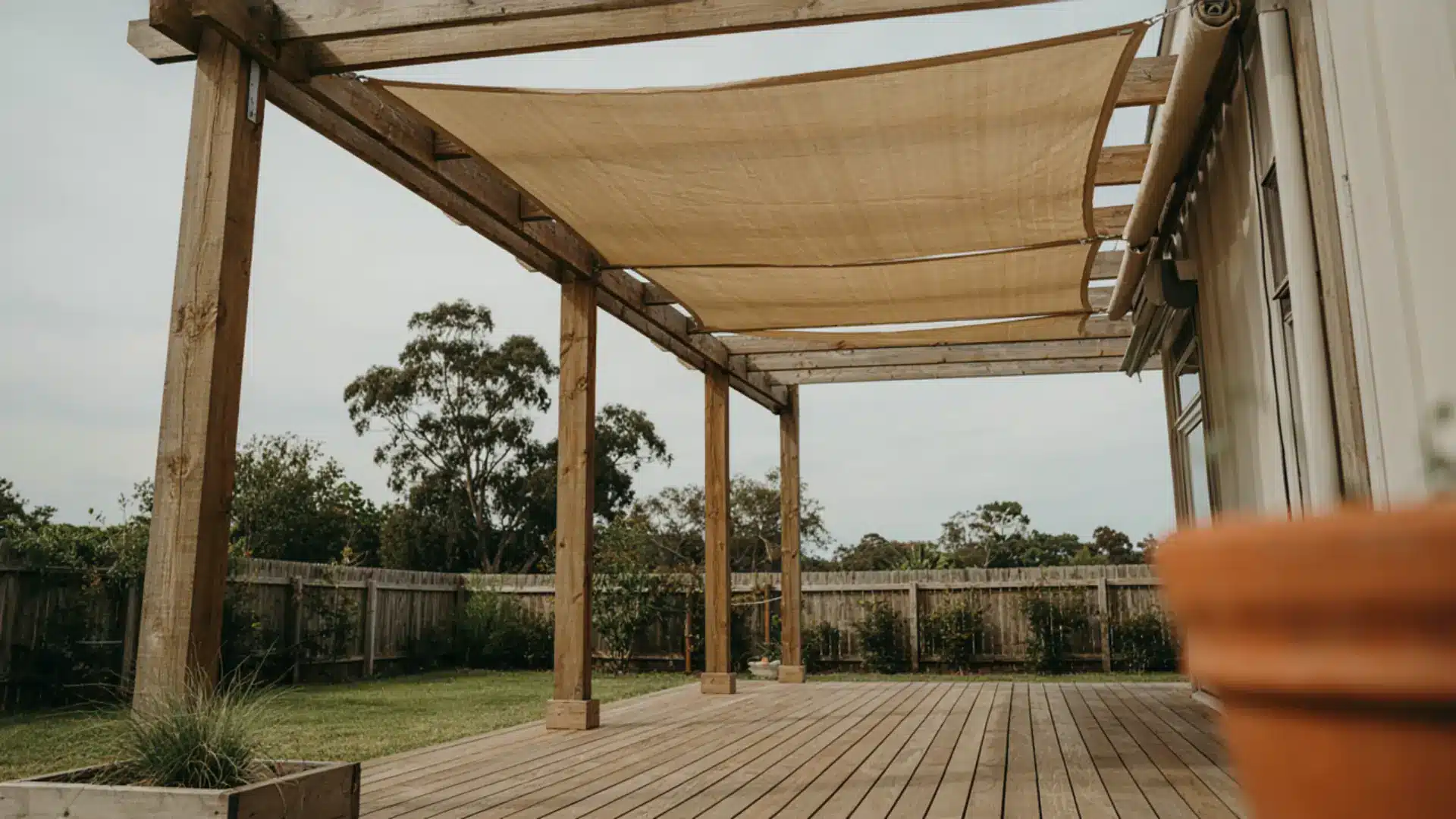 Wooden pergola fitted with a tan fabric shade sail canopy over a wooden deck.