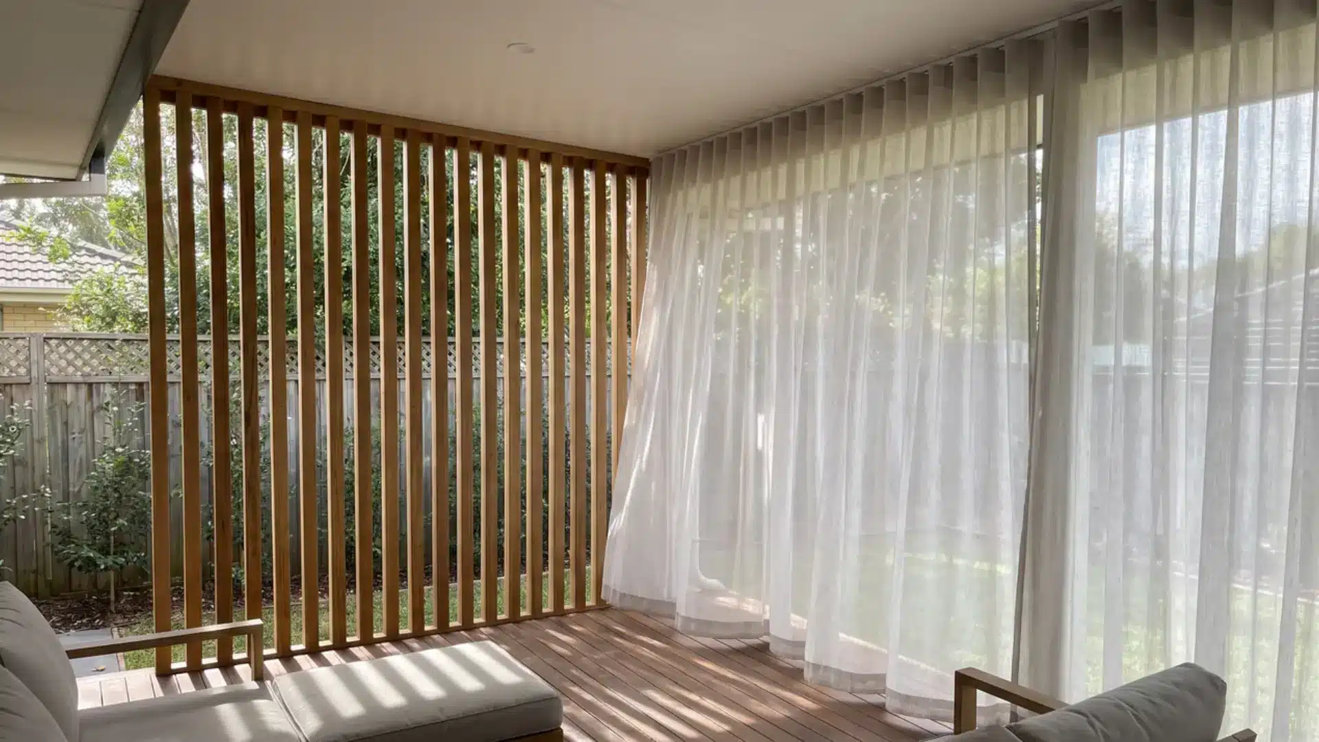 Covered wooden deck featuring vertical slat privacy screens and sheer white outdoor curtains.