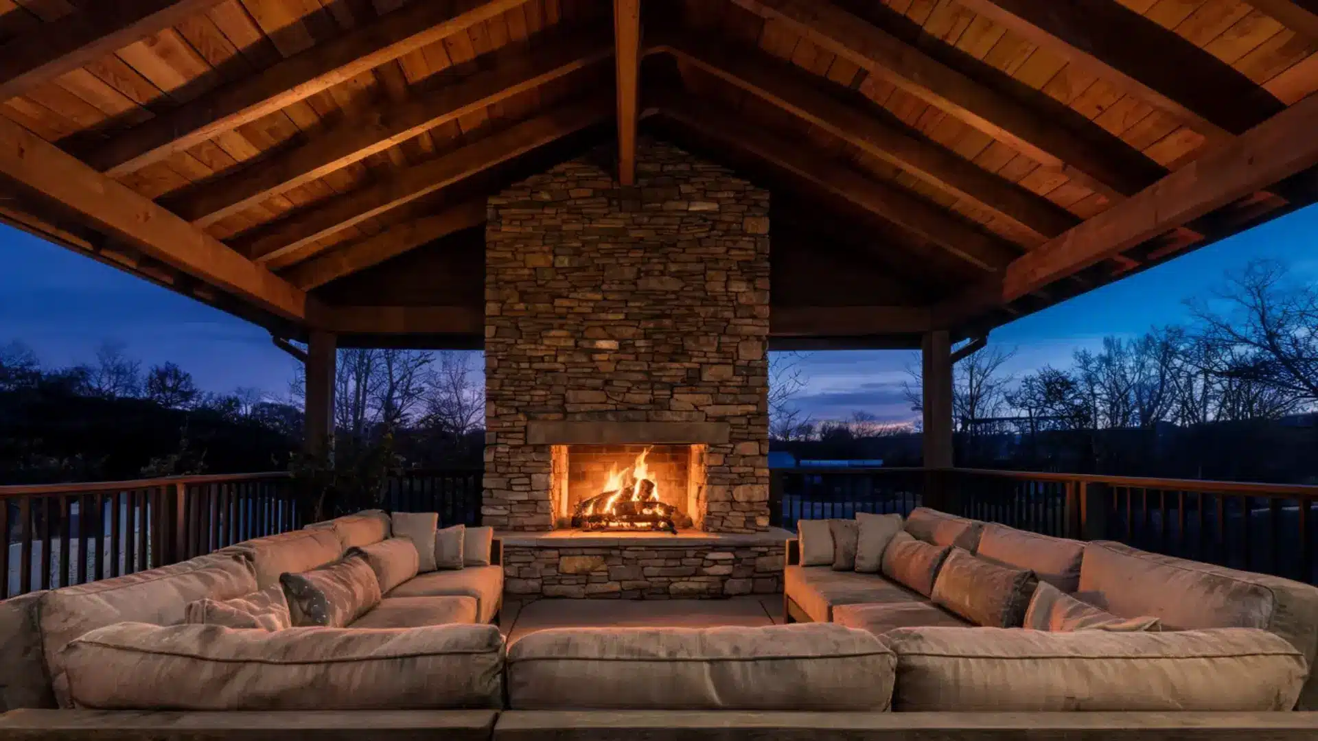 Covered deck with vaulted wooden ceiling featuring a large central stone fireplace and outdoor seating.
