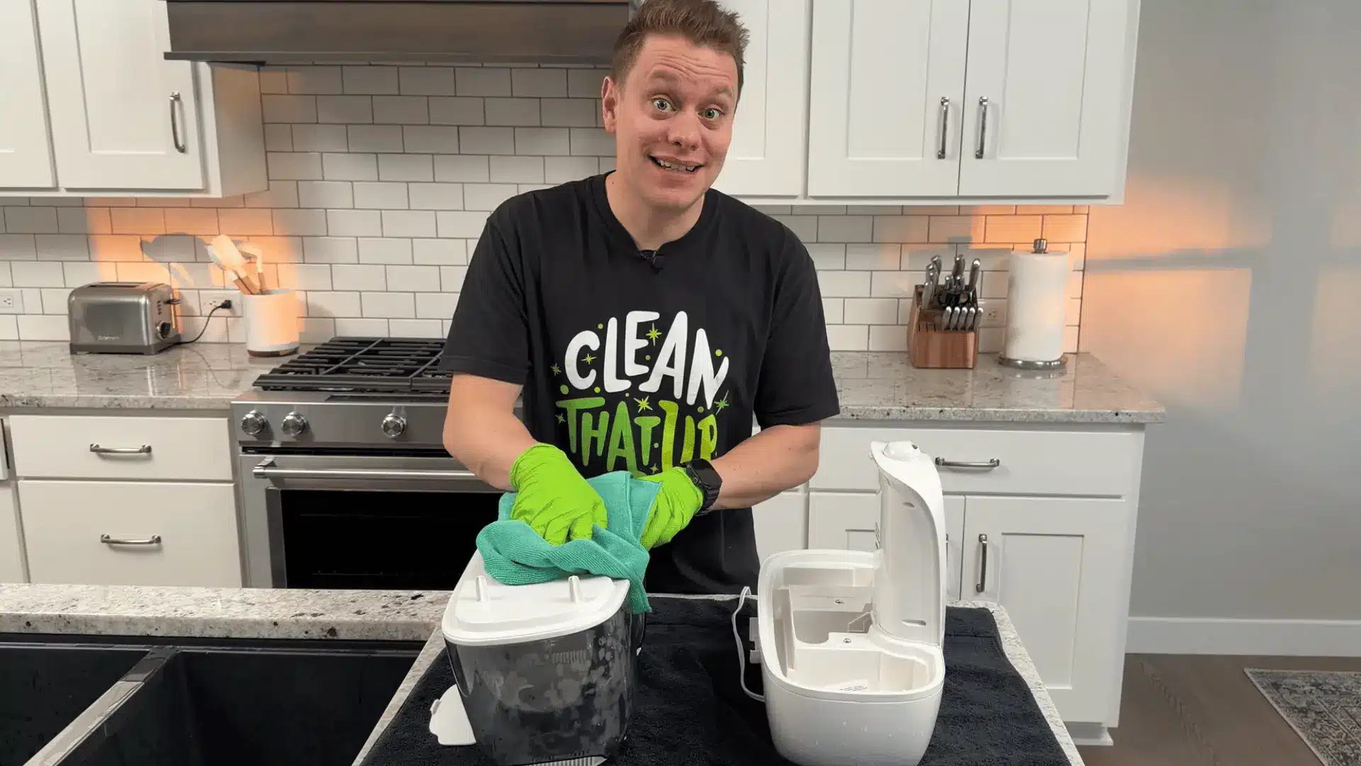Person cleaning a humidifier with gloves and a towel while disassembled parts sit on a kitchen counter.