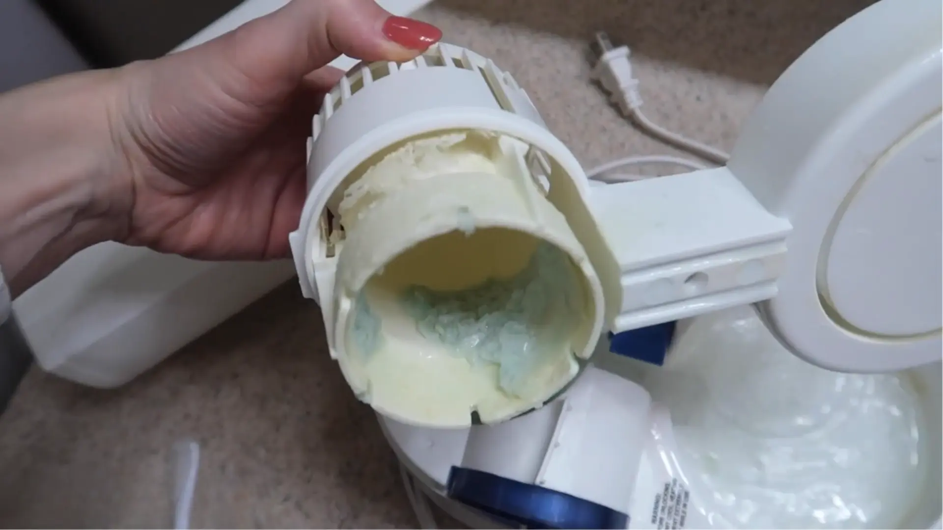 Hand holding a humidifier part coated with thick mineral scale before rinsing and cleaning.
