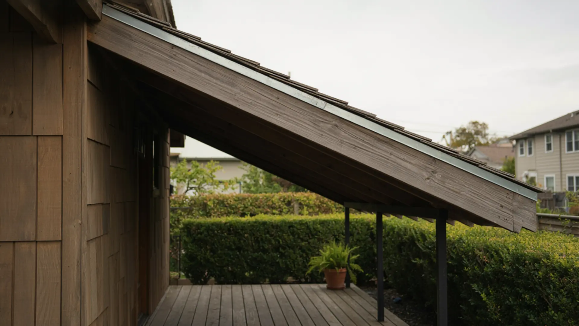 Wooden lean-to roof extension attached to a house side covering a deck area.