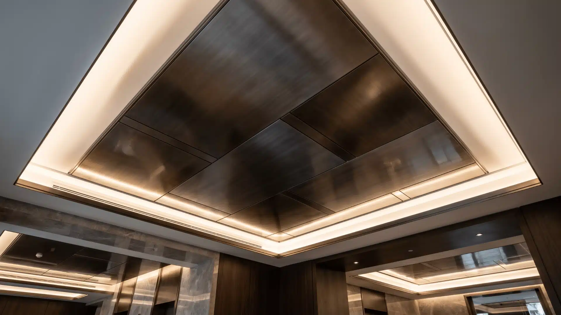 Metallic panel tray ceiling reflecting soft ambient light across recessed ceiling surface.