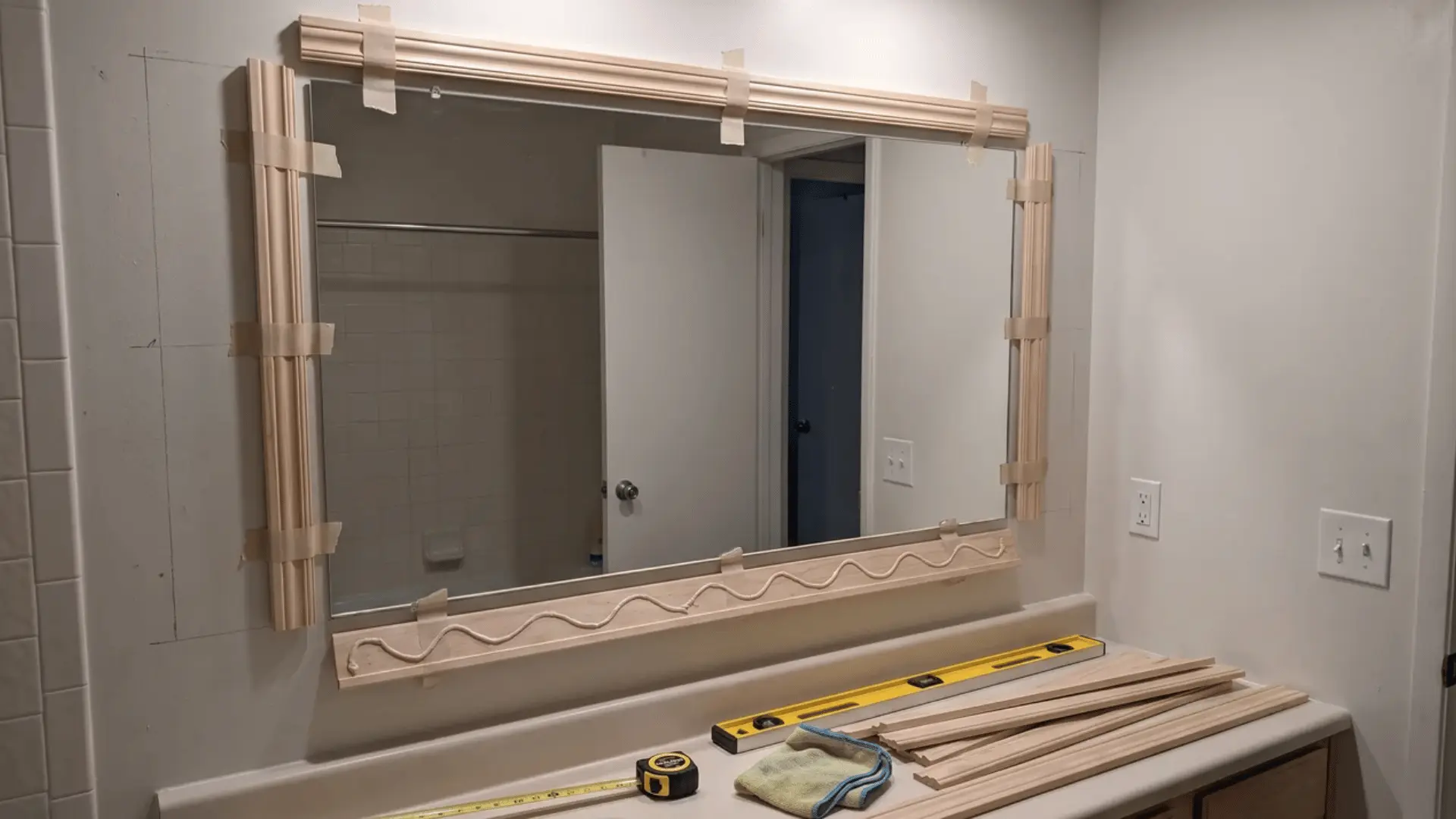 Bathroom mirror with molding pieces dry-fitted around the glass beside a level and measuring tape