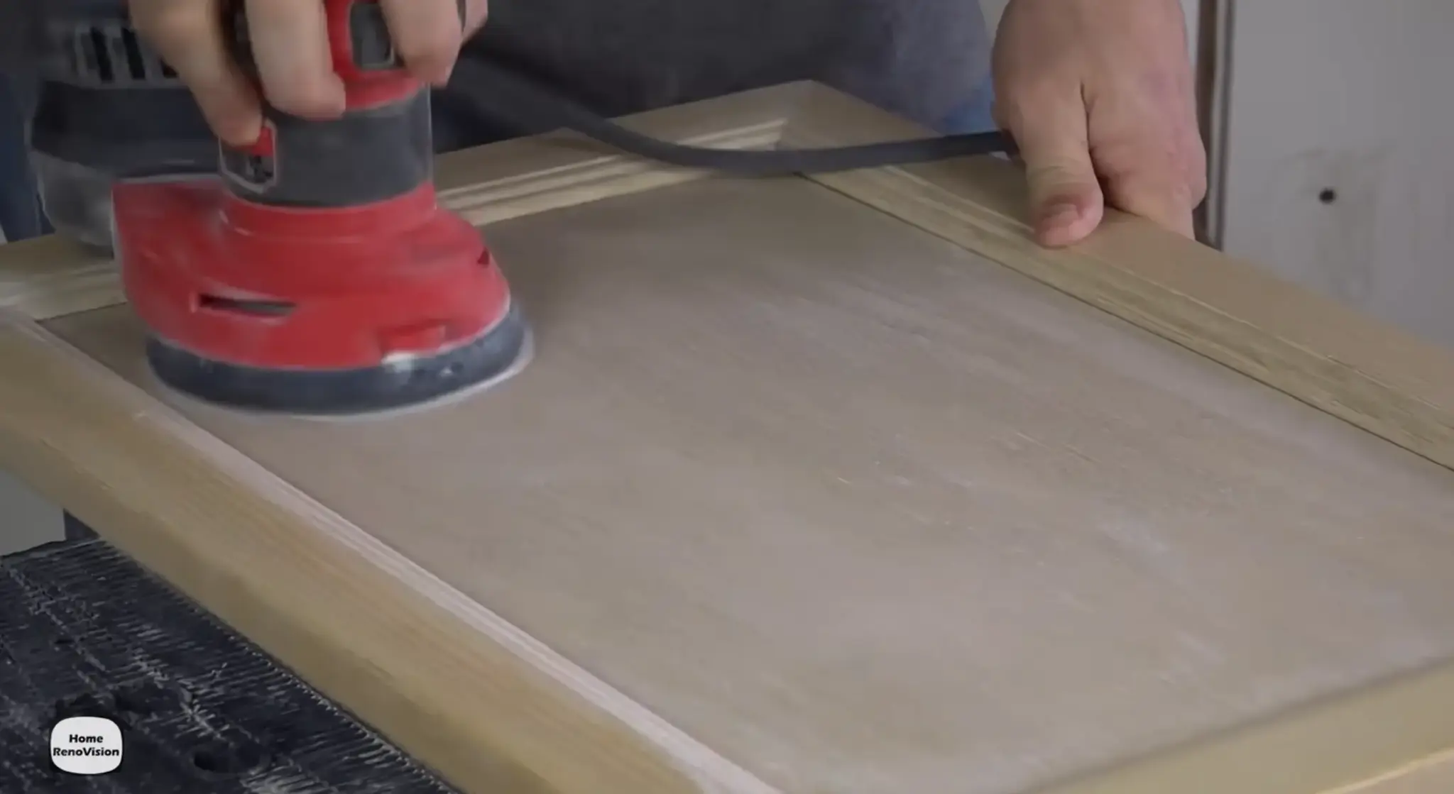 Scuff-sanding a wooden kitchen cabinet door with an orbital sander before applying bonding primer.