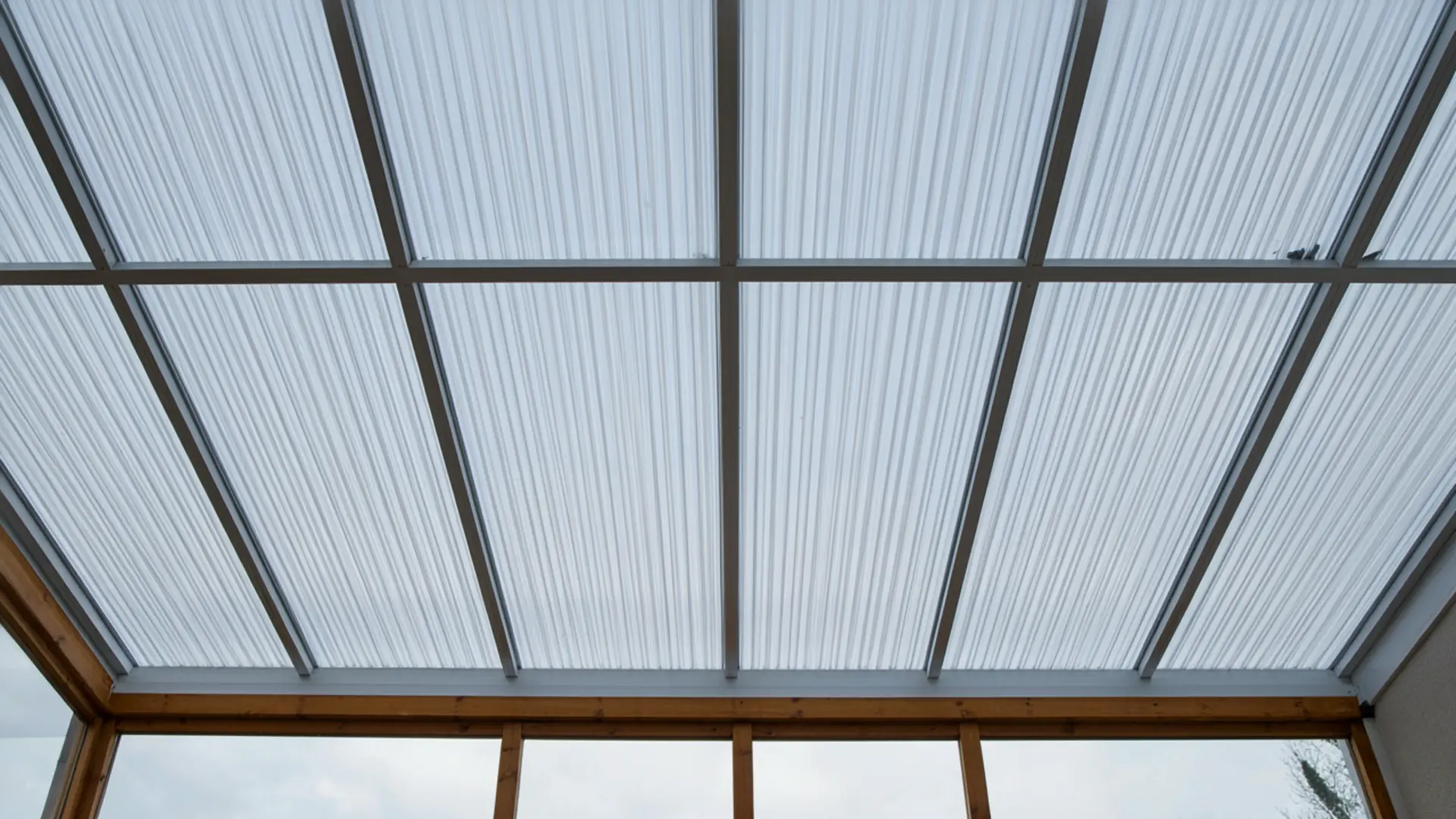 Translucent corrugated polycarbonate roof panels supported by a wooden patio frame structure.