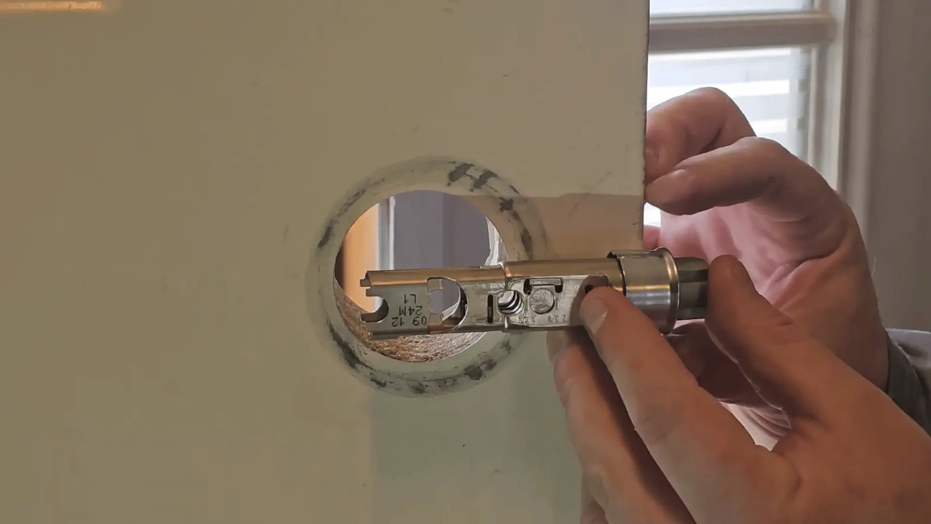 Close-up of hands inserting and adjusting a metal door latch assembly into a circular bore hole on a white interior door.