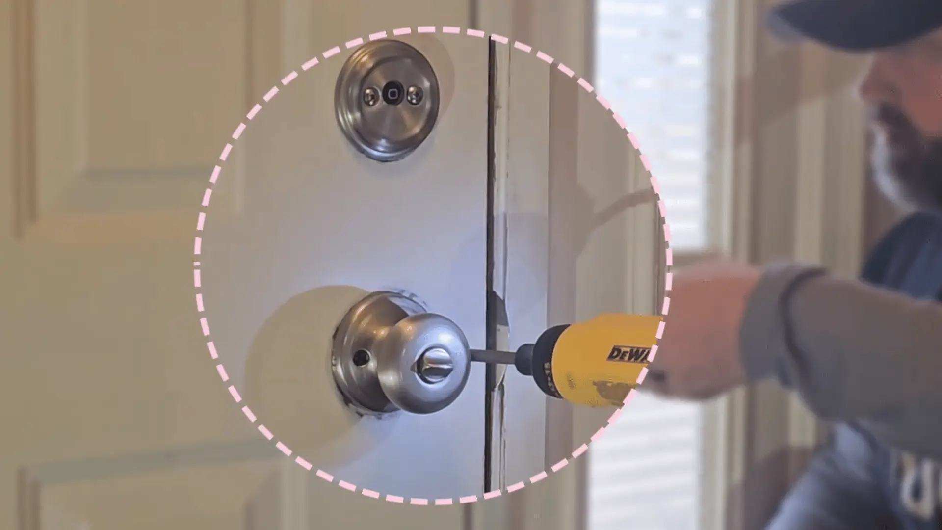 Worker using a drill to install a door lock and knob on a white interior door, highlighted with a dotted circle.