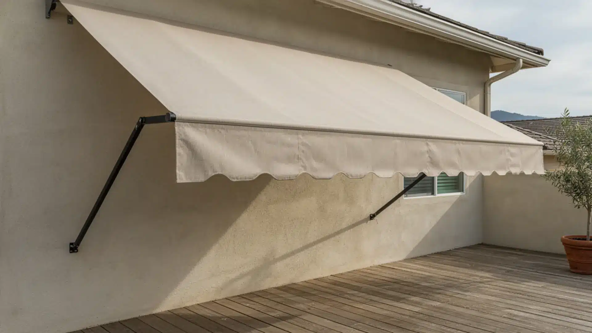 Beige fabric retractable awning extended over an outdoor wooden deck attached to a house.
