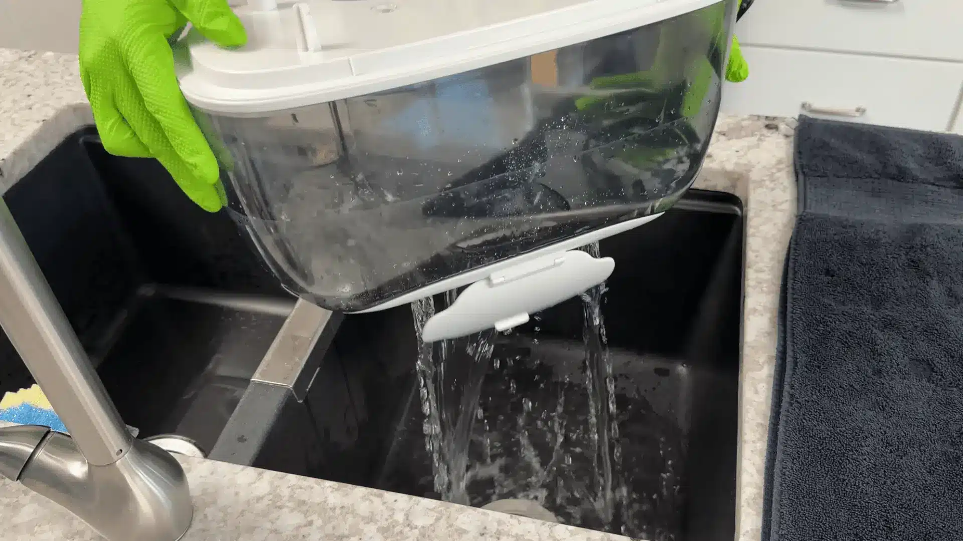 Person rinsing a humidifier base over a sink while cleaning internal parts with water.