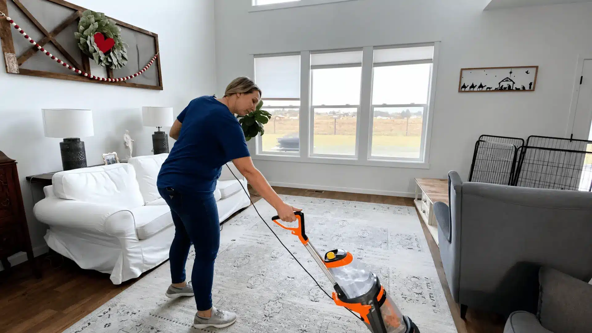 Woman shampooing a large area rug with a carpet cleaner in a bright living room before removing dirt and stains from the carpet.