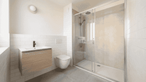 Small modern bathroom with wood vanity, wall-mounted toilet, and glass shower doors