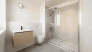 Small modern bathroom with wood vanity, wall-mounted toilet, and glass shower doors