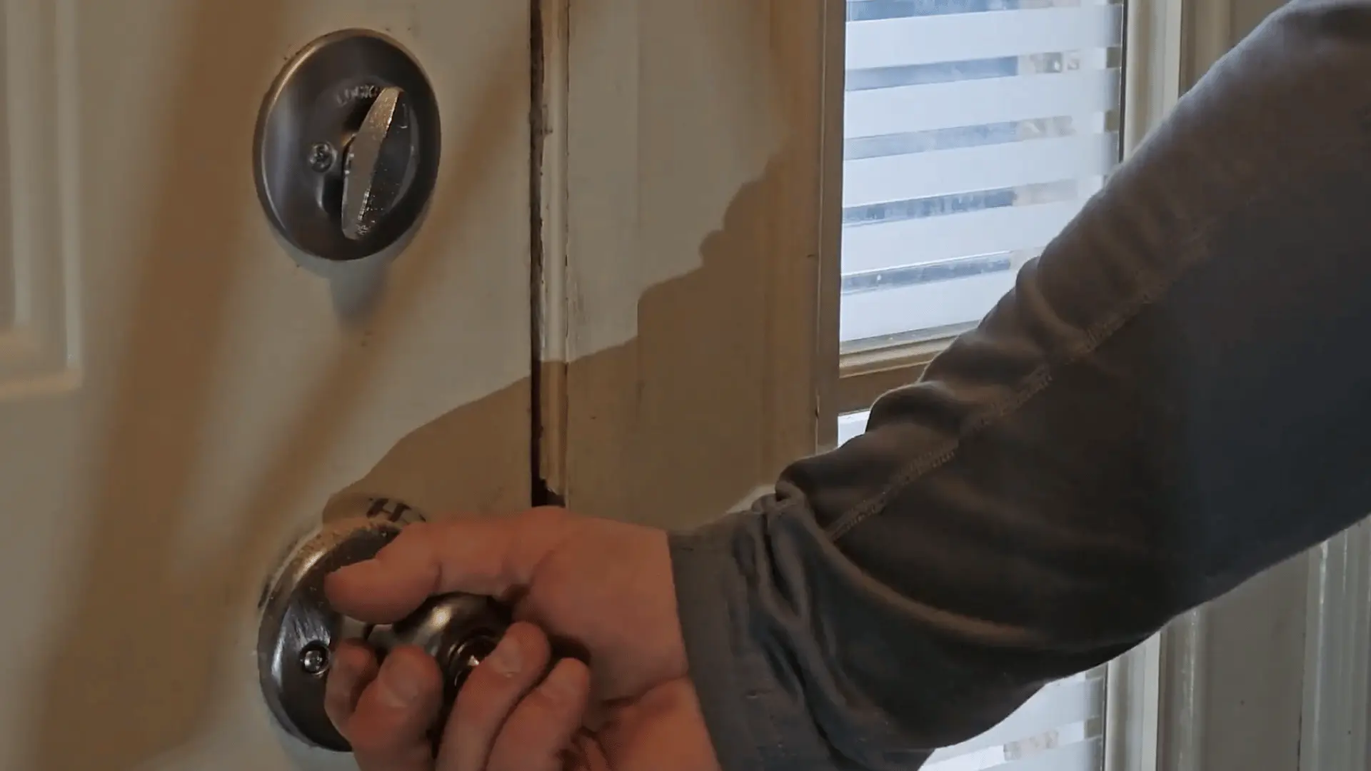 Hands testing and tightening a silver door knob on a white door after installation, checking latch alignment.