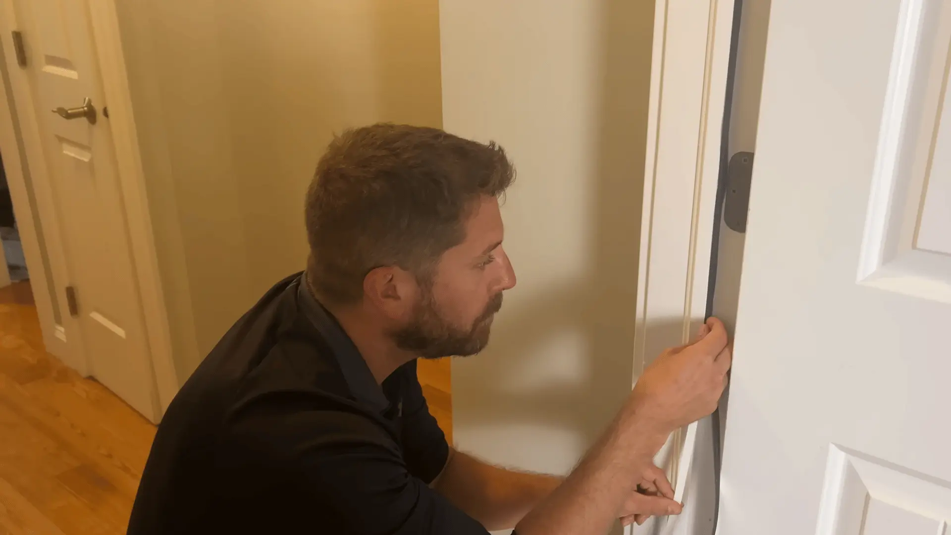 A man inspects and adjusts weatherstripping foam along the hinge side of an open white door.