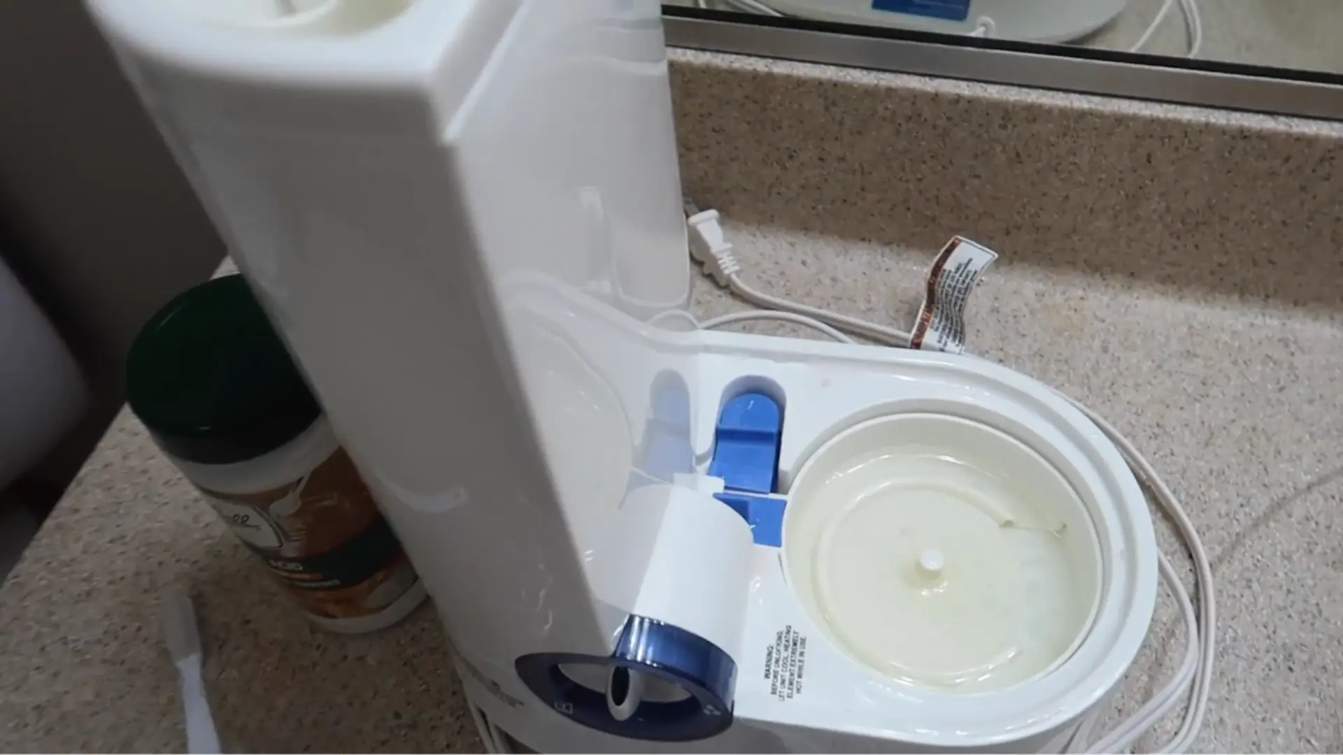 Unplugged warm-mist humidifier with the tank removed, exposing the base and heating chamber on a bathroom counter.