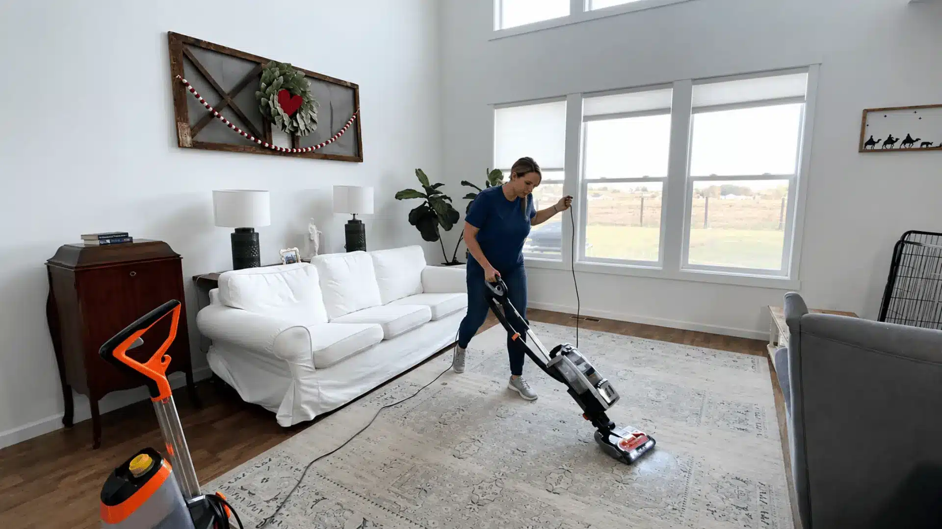Person vacuuming a large area rug with a carpet cleaning machine in a bright living room with natural daylight.