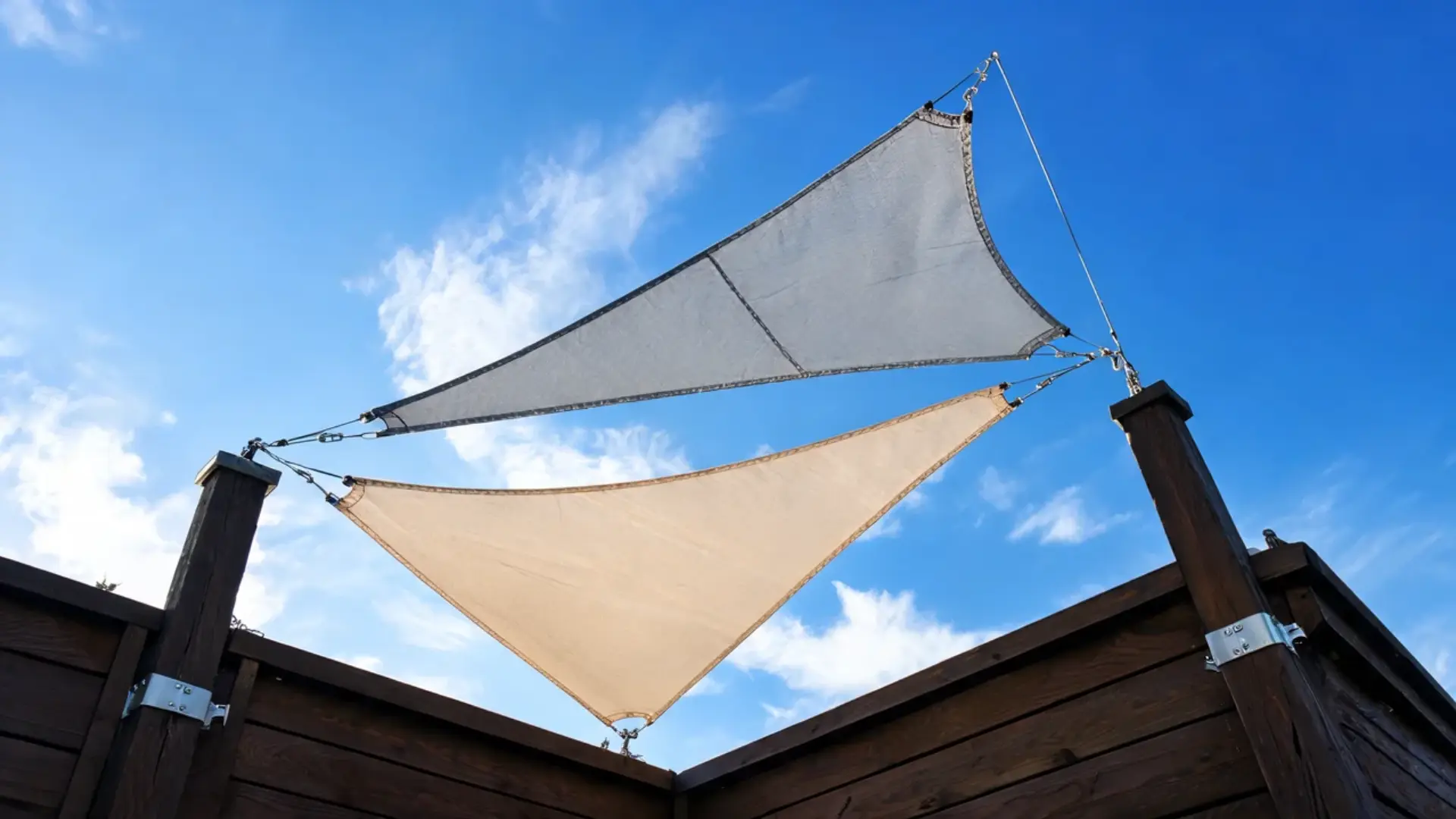 Triangular fabric shade sails mounted on wooden posts against a clear blue sky.