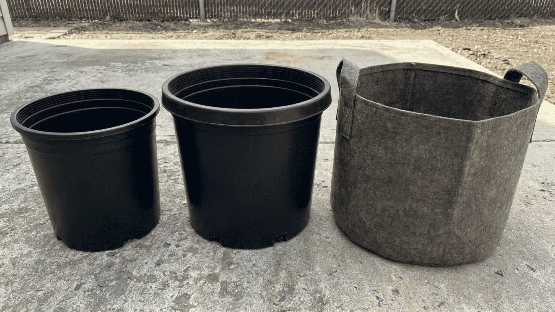 Three empty containers of increasing size, plastic pot, larger plastic pot, and fabric grow bag, on a flat surface
