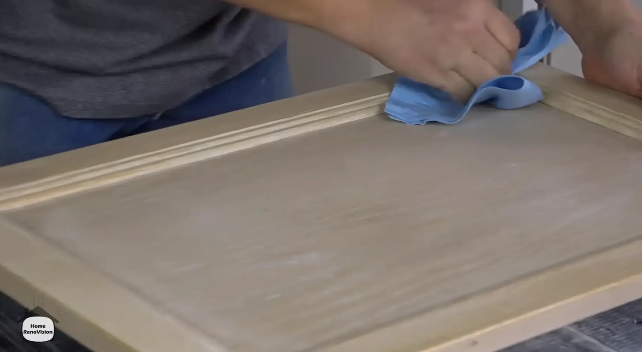 Wiping sanding dust from a wooden kitchen cabinet door with a clean cloth before applying primer.