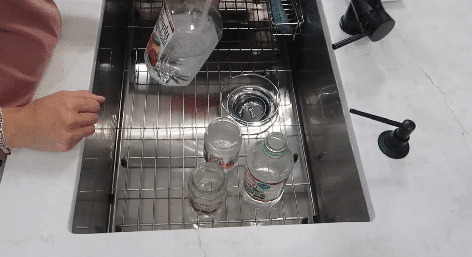 Several clear glass and plastic containers sitting in a kitchen sink as one bottle is held above them
