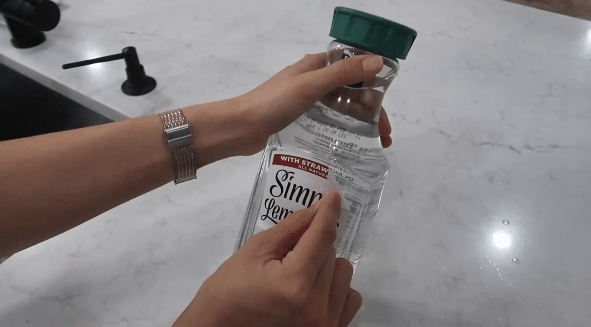 Hands peeling a label from the corner of a clear plastic bottle on a kitchen counter.