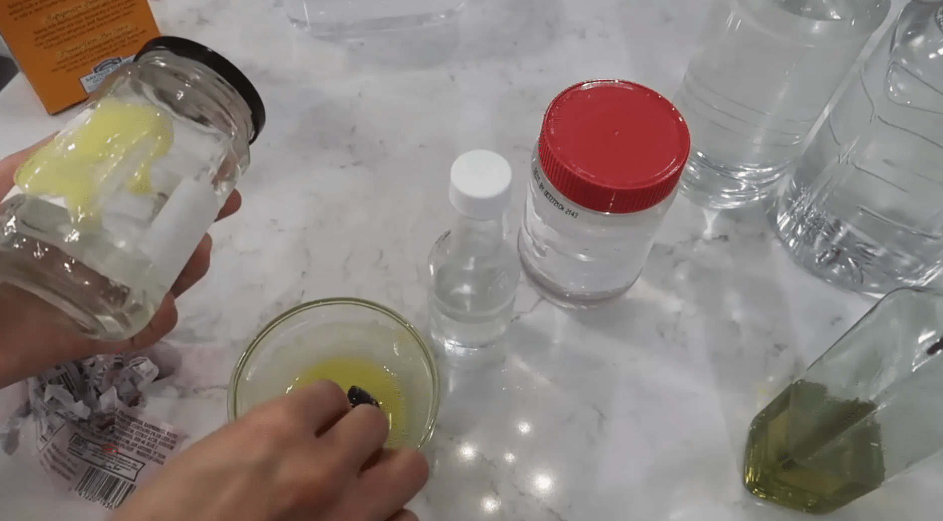 Baking soda and oil paste being rubbed onto a glass jar beside other clear containers on a counter